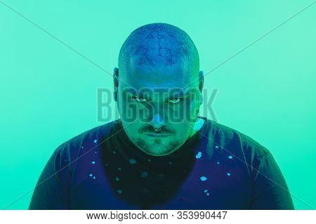 Threat. Portrait Of A Guy With Colorful Neon Light On Green Studio Background. Male Model With Calm,