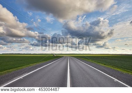 Empty Asphalt Highway Outside The City Among Green Fields And Against A Beautiful Cloudy Sky