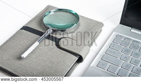 Magnifying Glass At Notebook With Open Laptop. Schedule, Agenda Analysis, Planning. High Quality Pho