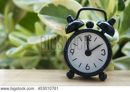 Black Alarm Clock Isolated On Blurred Nature Background. The Clock Set At 2 O'clock. Copy Space.