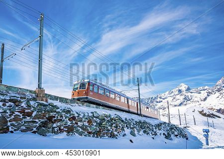 Famous Red Train Running Towards Gornergrat Station On Mountain Against Sky