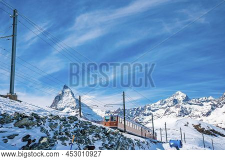 Red Train Passing Through Snowy Matterhorn Mountain Against Sky During Winter