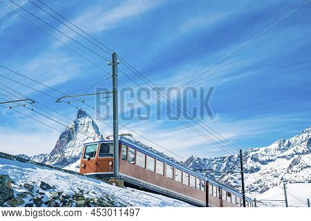 Red Train Running Towards Gornergrat Station On Snowy Mountain Against Sky