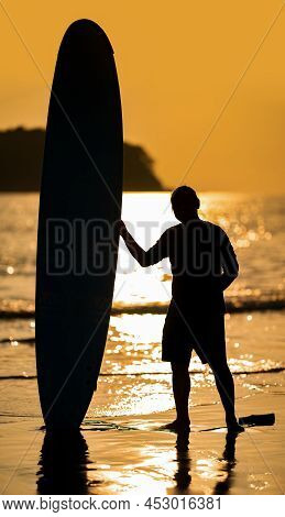 Silhouette Smart Asian Man Long Hair Touches And Poses With Standed Surfboard On The Beach In Twilig