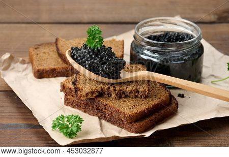 Fresh Grainy Black Paddlefish Caviar In Brown Wooden Spoon On A Brown Table, Close Up