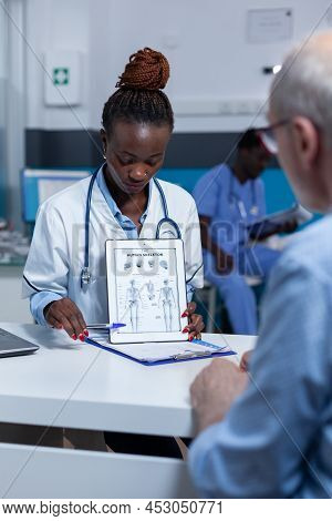 Clinic Medic Specialist Showing Diagram Of Human Body To Senior Patient. Doctor Explaining Retired M