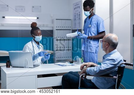 General Practitioner Explaining Illness Symptoms To Senior Patient With Disability While Hospital Nu