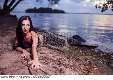 Sexy Seducing Mermaid Posing With Net Near Sea On Rocks While Wearing Artistic Makeup And Black Shin