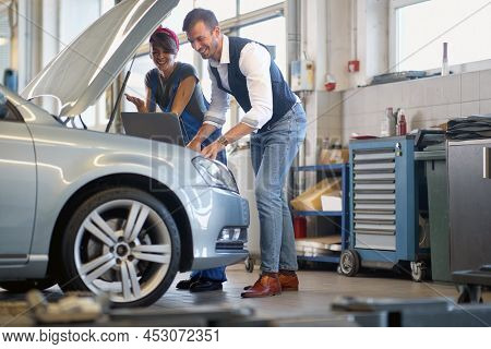 Cheeerful man and woman working in car workshop