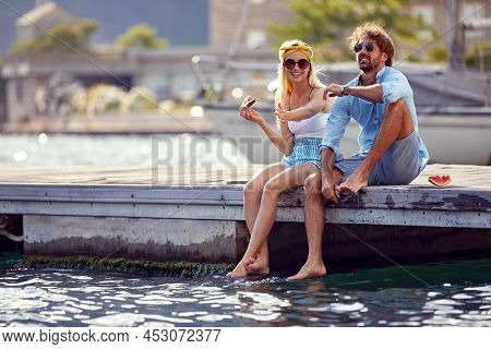 Happy  man and girl sitting on the lake pier dangling legs and eating watermalon