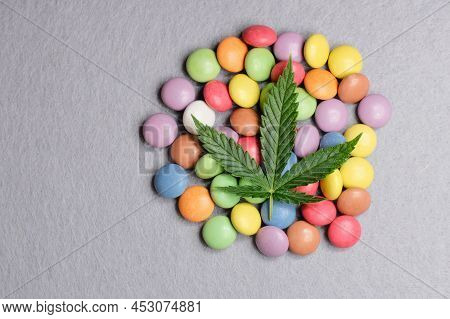 Cannabis Leaf With Colorful Candy Confetti Close Up. Marijuana Sweets With Cbd And Thc On Gray 
Back