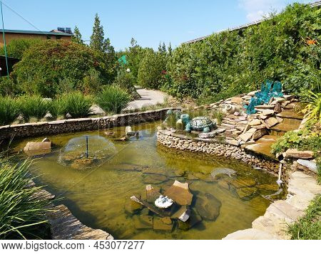 Beautiful Fountain With Rocks And Waterfalls. Fountain In The Park Near Big Green Trees