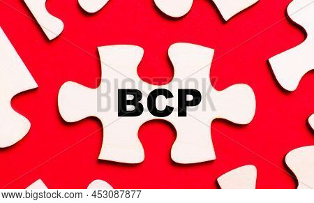 On A Bright Red Background, White Puzzles. In One Of The Pieces Of The Puzzle, The Text Bcp Business