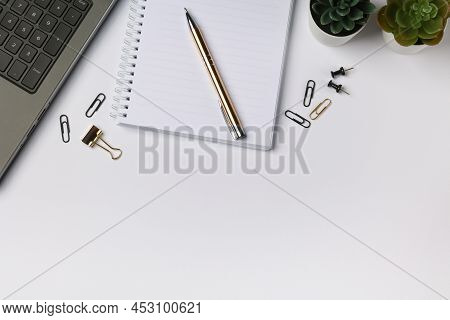 Top View Of Light Working Place With Grey Laptop, White Notebook And Gold Colored Pen On It, Black A