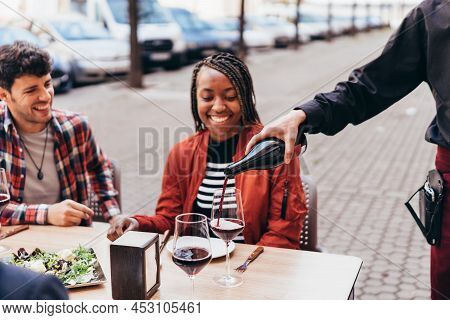 Waiter Serving Red Wine To A Smiling Black Woman With Braids