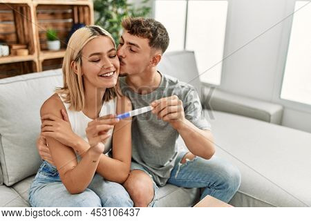 Young caucasian couple smiling happy holding pregnacy test at home.