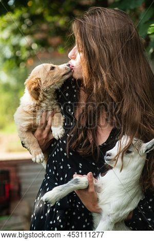 Woman Hugging Pet Puppy Dog And Goatling Yeanling. Natural Young Woman. Virgin Girl In Village. Spri