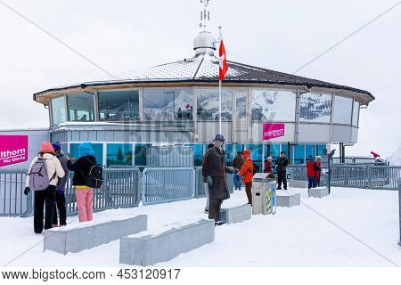 Lauterbrunnen, Switzerland - November 7, 2019: Tourists Observing On Snowy Deck Outside Glass Buildi