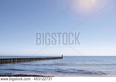 Beautiful Seaside Background, Wooden Breakwater In Calm Sea Against Clear Blue Sky