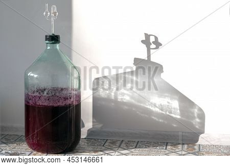 The Process Of Making Red Homemade Wine. A 20 Liter Glass Bottle With An Airlock In A Cork. Fermenta