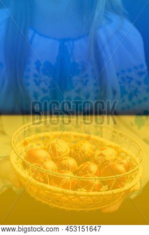 Defocus Ukrainian Girl In Vyshyvanka Holding Basket Of Colored Red Eggs On Nature Green Grass Backgr