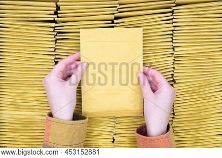 Top View Of Female Hands Holding A Padded Envelope Over Batch Of Stacked Yellow Bubble Mailers, Copy