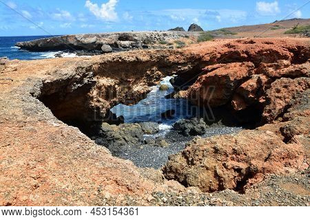 Natural Rock Bridge On Black Stone Beach Along The Coast Of Aruba.