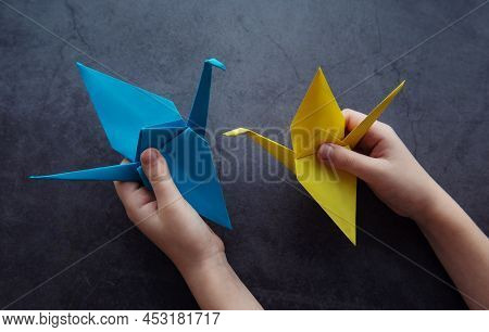 Girl's Hands Hold Paper Cranes In The Colors Of The Ukrainian Flag On A Black Background. Support Fo
