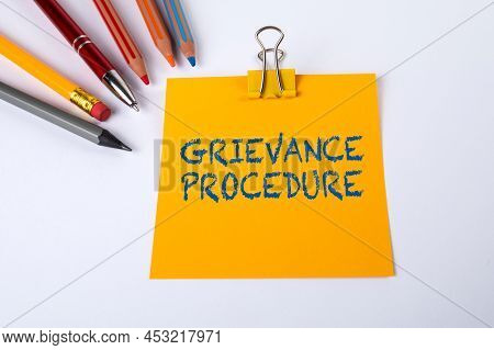 Text Grievance Procedure On Yellow Piece Of Paper. White Office Desk