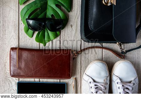 Black Bag, White Sneakers Travel Holder, Sunglasses And Greean Leaf On The Wooden Background