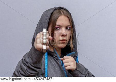 A Teenage Girl Strikes With Brass Knuckles On A Light Background, Wearing A Hoodie With A Hood. Conc
