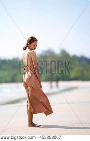 Beautiful Relaxed Thai Woman Poses On The Beach In The Sunlight  With Happiness And Relaxation.