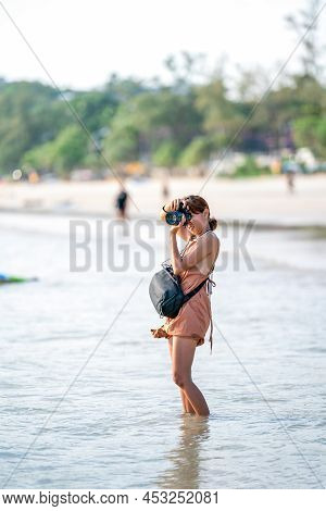Smart Asian Woman Takes A Photo With Her Digital Camera On The Beach In Afternoon Sunlight.