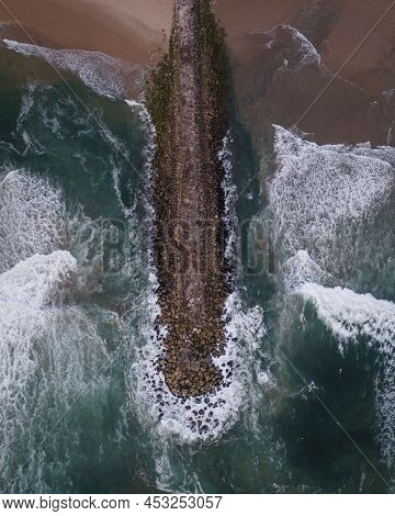 Aerial View Of A Majestic Breakwater With Rough Rolling Water Waves Rolling On The Beach At Costa Da