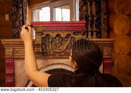 Lady Painting Carved Ornaments Of Antique Wooden Cupboard For Kitchen With Window In Background. Re-