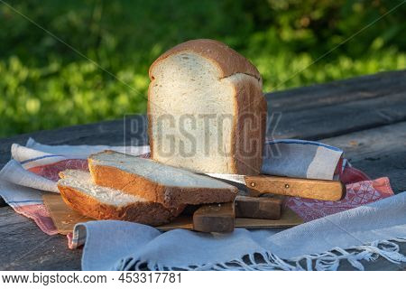 A Freshly Baked Loaf Of White Wheat Bread On A Wooden Table In The Garden. Thick Slices Of Bread Cut
