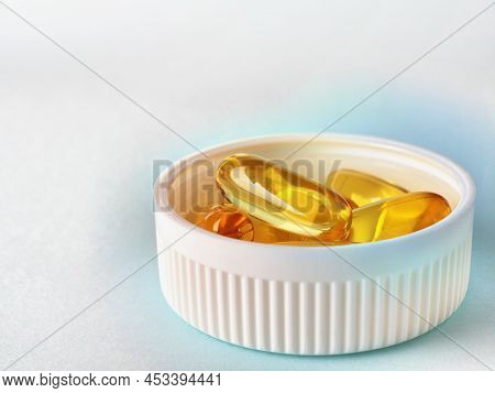Fish Oil. Yellow Softgels Or Capsules Are In Bottle Cap. Blue And White Surface. Vitamins And Health