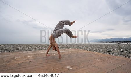 Shirtless Caucasian Man Doing Backflip On Pebble Beach.