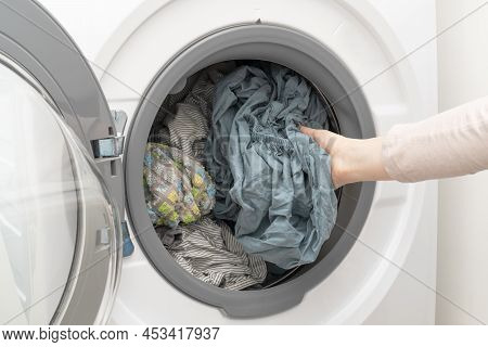 Clean Wet Laundry Inside Of Washing Machine. Woman's Hand Pulling Out Washed Clothes From The Drum.