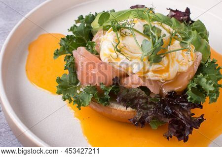 Restaurant Dish Brioche With Poached Egg With Salmon And Avocado. Delicious Bread With Greens