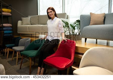 Charming Sales Assistant In Casual Clothes, Standing Near Velour Stylish Chairs In The Furniture Sho