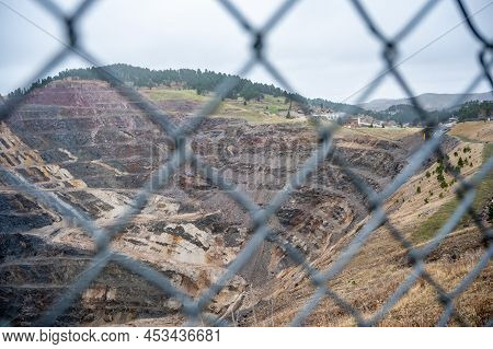 Open Pit Mine In Background With A Blurred Chain Link Fence In The Foreground.