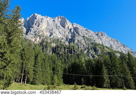 The View Of A Mountain Massif Through Green Forest In A Sunny Day. Malga Ciapela, Veneto, Italy.