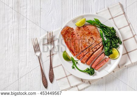 Fried Tuna Steak With Parboiled Broccolini And Lime On White Plate On White Textured Wooden Table, H