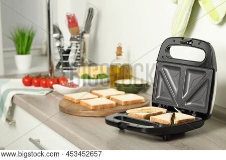 Modern Sandwich Maker With Bread Slices On Wooden Table In Kitchen