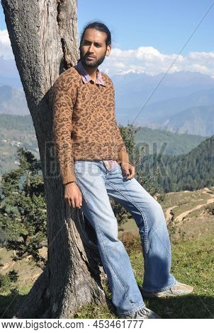 Full Length Of A Good Looking South Asian Young Men Looking Sideways While Leaning Against Tree In H
