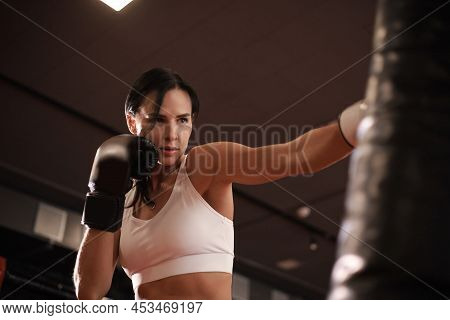 Young Woman Boxer Athletic Wearing Gloves Strikes Punching Bag During Training Preparation For Battl