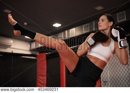 Young Woman Trains In Kickboxing Ring With Heavy Punching Bag. Foot Kicks Or Knee Strike.