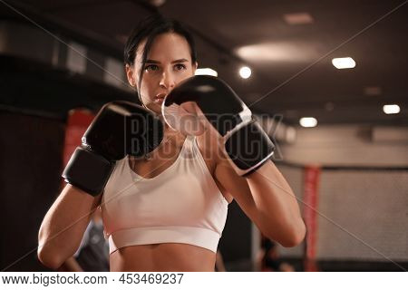 Female In Boxing Gloves And Sportive Wear Stands In A Rack In The Boxing Hall