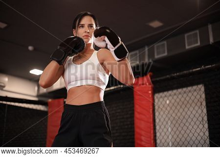 Female In Boxing Gloves And Sportive Wear Stands In A Rack In The Boxing Hall